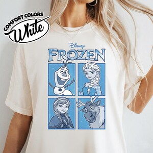 May include: White t-shirt featuring the Disney movie "Frozen" characters Olaf, Elsa, Anna, and Sven in a blue and white design. The shirt also has the words "Comfort Colors" and "White" printed on it.