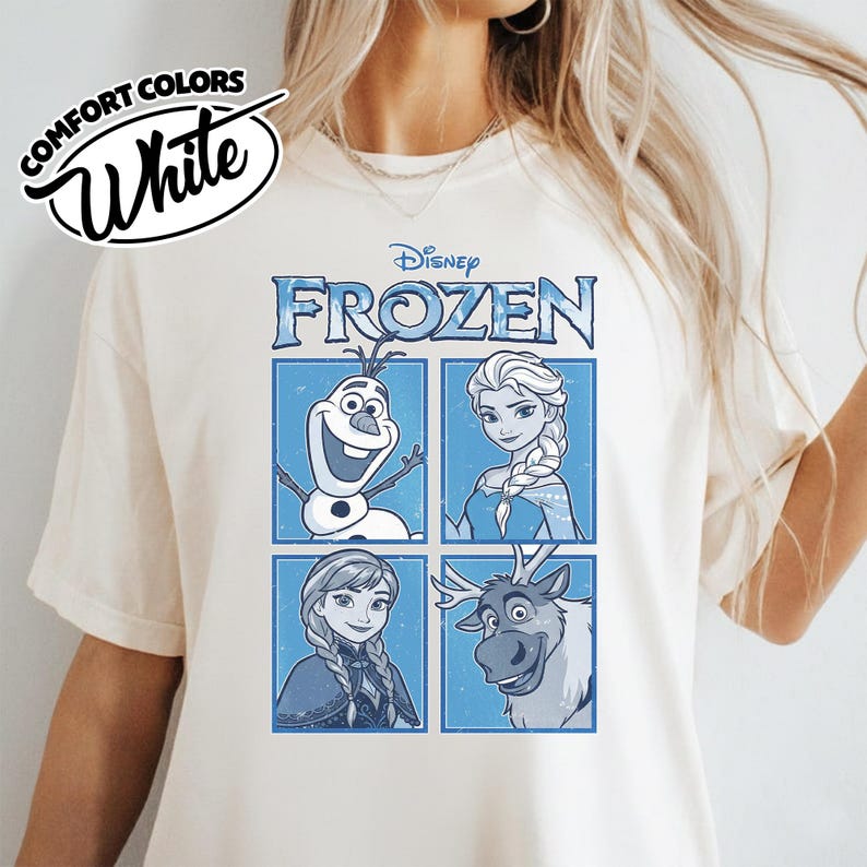 May include: White t-shirt featuring the Disney movie "Frozen" characters Olaf, Elsa, Anna, and Sven in a blue and white design. The shirt also has the words "Comfort Colors" and "White" printed on it.