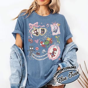 K&ouml;nnte beinhalten: Blaues Comfort Colors T-Shirt in Jeansoptik mit einer farbenfrohen Grafik verschiedener Spider-Man-Charaktere in verzierten Rahmen und einem Spinnennetz-Design. Das Shirt hat hochgekrempelte &Auml;rmel und den Text "COMFORT COLORS Blue Jean".