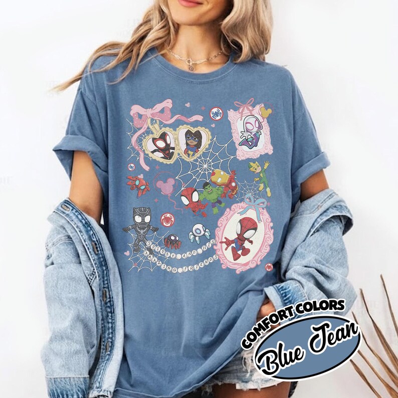 K&ouml;nnte beinhalten: Blaues Comfort Colors T-Shirt in Jeansoptik mit einer farbenfrohen Grafik verschiedener Spider-Man-Charaktere in verzierten Rahmen und einem Spinnennetz-Design. Das Shirt hat hochgekrempelte &Auml;rmel und den Text "COMFORT COLORS Blue Jean".