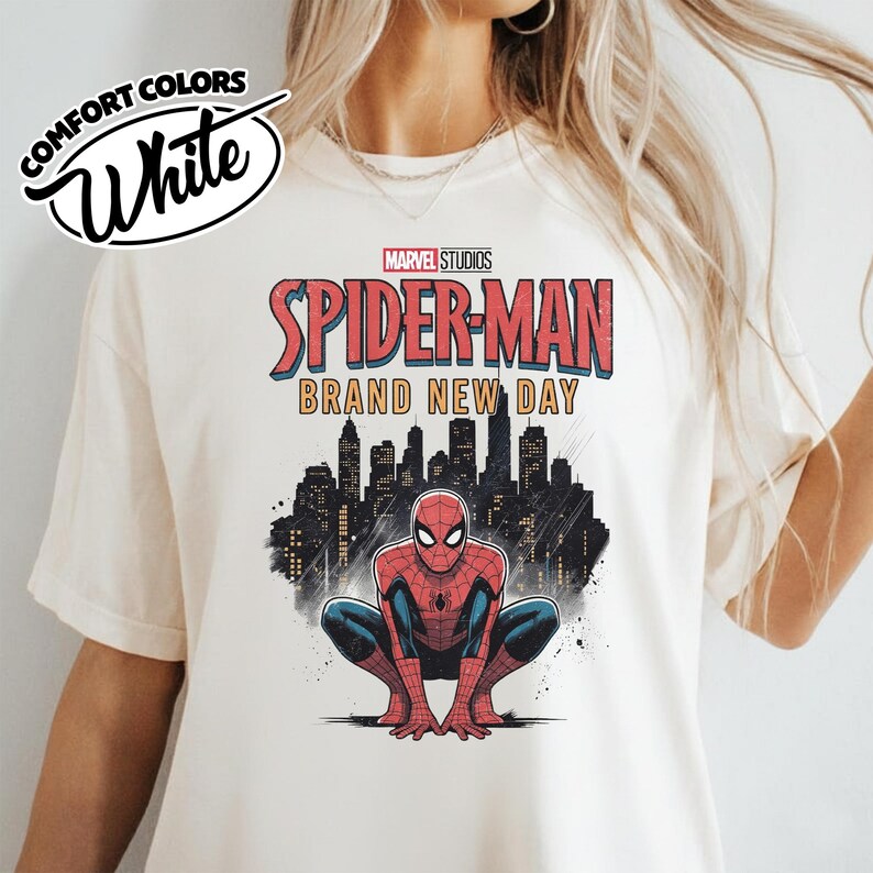 Puede incluir: Una camiseta blanca con un estampado gr&aacute;fico de Spider-Man en cuclillas. Sobre el personaje, el texto dice Marvel Studios Spider-Man Brand New Day en rojo y amarillo. Detr&aacute;s se ve la silueta negra de un horizonte urbano.