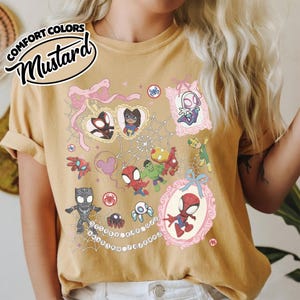 K&ouml;nnte beinhalten: Senffarbenes T-Shirt mit einer farbenfrohen Grafik von Spider-Man und seinen Freunden. Das Design umfasst verschiedene Charaktere, Spinnennetze und den Text "Spidey and his friends". Das Shirt hat eine lockere Passform und die Worte "Comfort Colors" sind oben links aufgedruckt.