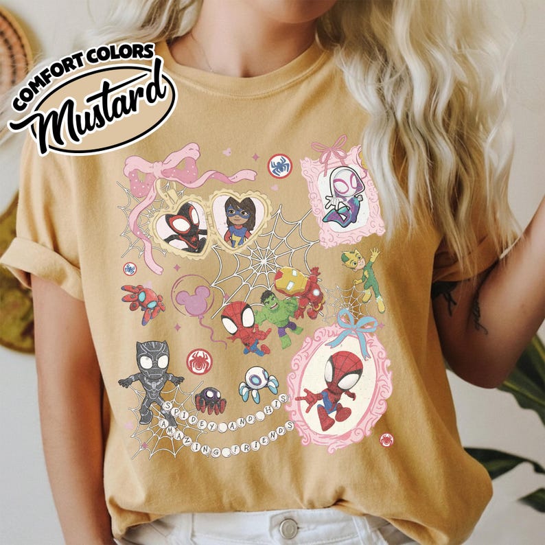 K&ouml;nnte beinhalten: Senffarbenes T-Shirt mit einer farbenfrohen Grafik von Spider-Man und seinen Freunden. Das Design umfasst verschiedene Charaktere, Spinnennetze und den Text "Spidey and his friends". Das Shirt hat eine lockere Passform und die Worte "Comfort Colors" sind oben links aufgedruckt.