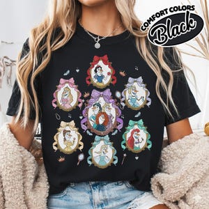 May include: Black t-shirt featuring framed portraits of animated characters. Each portrait is surrounded by a decorative bow. The shirt has the words "Comfort Colors Black" printed on the upper right side.