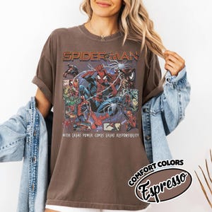 K&ouml;nnte beinhalten: Espressofarbenes T-Shirt mit einem Spider-Man-Motiv. Das Design zeigt den Text "SPIDER-MAN" oben, mit Comic-Panels von Spider-Man. Der Satz "WITH GREAT POWER COMES GREAT RESPONSIBILITY" ist darunter gedruckt. Das Shirt ist eine Komfort-Passform.