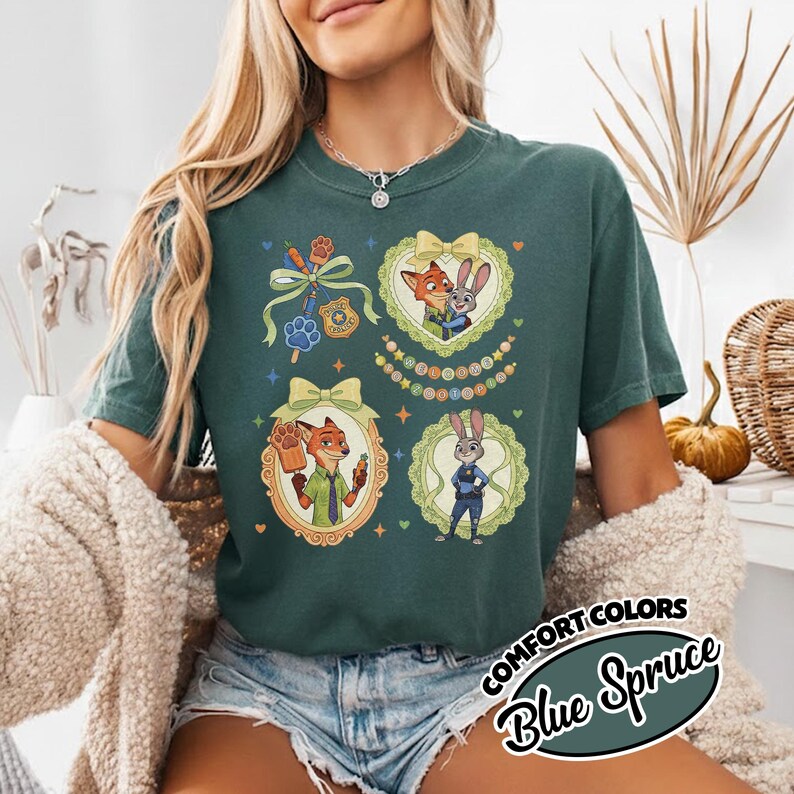May include: A dark green short-sleeve t-shirt featuring a graphic print of two animated characters, a fox and a rabbit, framed by decorative borders with bows. The design includes a police badge, a paw print, and small colorful stars and hearts.