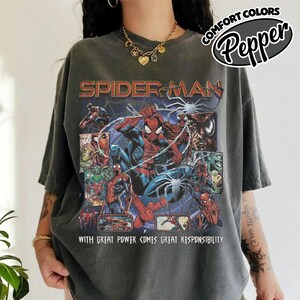 K&ouml;nnte beinhalten: Dunkelgraues T-Shirt mit einem Spider-Man-Motiv. Das Design zeigt mehrere Bilder von Spider-Man, den Text "SPIDER-MAN" und "WITH GREAT POWER COMES GREAT RESPONSIBILITY". Das T-Shirt hat kurze &Auml;rmel und eine lockere Passform.
