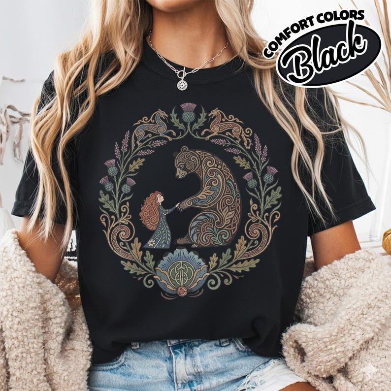 May include: Black t-shirt with a circular design featuring a bear and a girl holding hands, surrounded by floral and animal motifs. The text "COMFORT COLORS Black" is printed on the upper right. The design is in shades of brown, green, and blue.