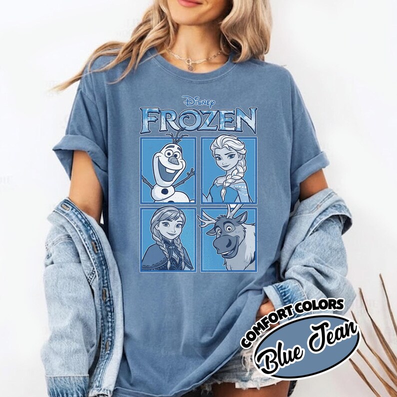 May include: Blue jean-colored t-shirt featuring the Disney Frozen logo and character illustrations in a four-panel grid. The shirt includes Olaf, Elsa, Anna, and Sven. The text "COMFORT COLORS Blue Jean" is printed on the bottom right.