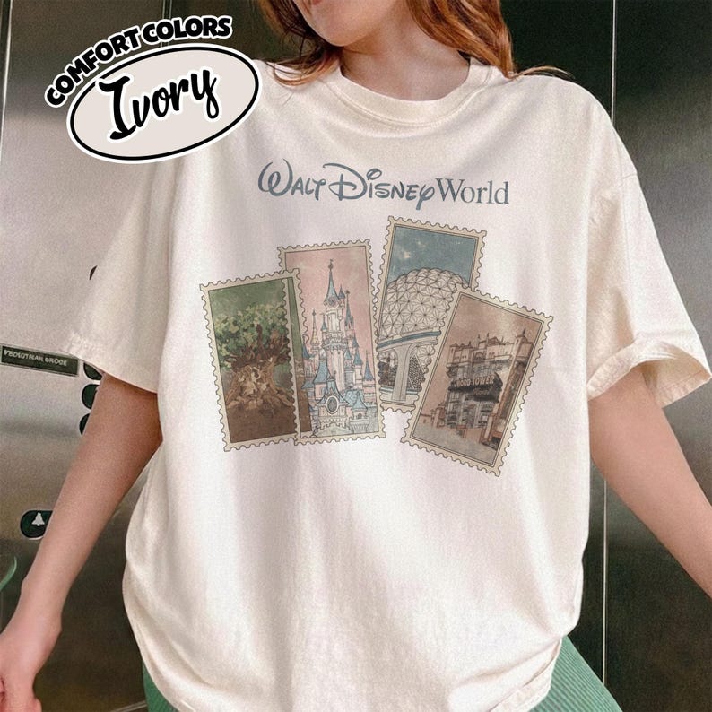Op de afbeelding: Ivoor kleurig T-shirt met de tekst "Walt Disney World" in een lichtblauwe letter. Het shirt heeft vier postzegel-achtige afbeeldingen van Disney World attracties. De linkerbovenhoek van het shirt heeft een Comfort Colors logo met het woord "Ivory".