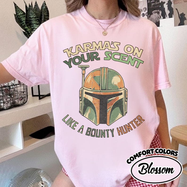 May include: Pink t-shirt with a graphic of a bounty hunter helmet and the text "Karma's on Your Scent Like a Bounty Hunter." The shirt is from Comfort Colors, Blossom.