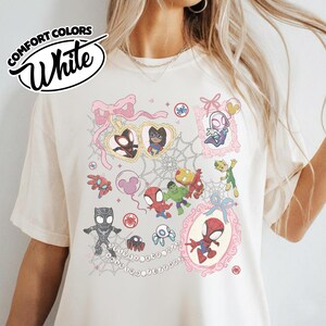 K&ouml;nnte beinhalten: Wei&szlig;es Comfort Colors T-Shirt mit einer farbenfrohen Grafik verschiedener Spider-Man-Charaktere und verwandter Elemente. Das Design umfasst gerahmte Portr&auml;ts, Spinnennetze und den Text "Spidey and his friends".