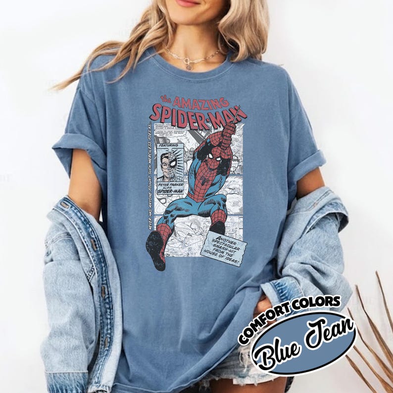 K&ouml;nnte beinhalten: Blaues Jeans Comfort Colors T-Shirt mit einem Vintage-Comic-Grafik von Spider-Man. Die Grafik enth&auml;lt den Text "The Amazing Spider-Man" und Comic-Panels. Das Shirt hat hochgekrempelte &Auml;rmel.