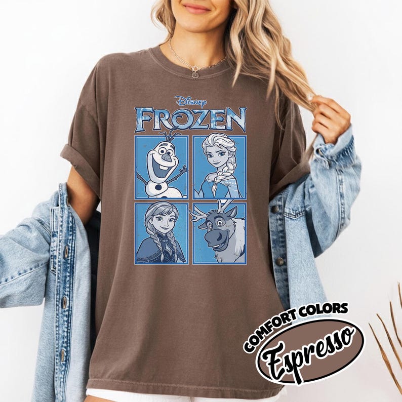 May include: Brown t-shirt featuring the Disney movie "Frozen." The shirt displays four character portraits in blue squares: Olaf, Elsa, Anna, and Sven. The text "FROZEN" is above the portraits. The shirt also has the text "COMFORT COLORS Espresso."