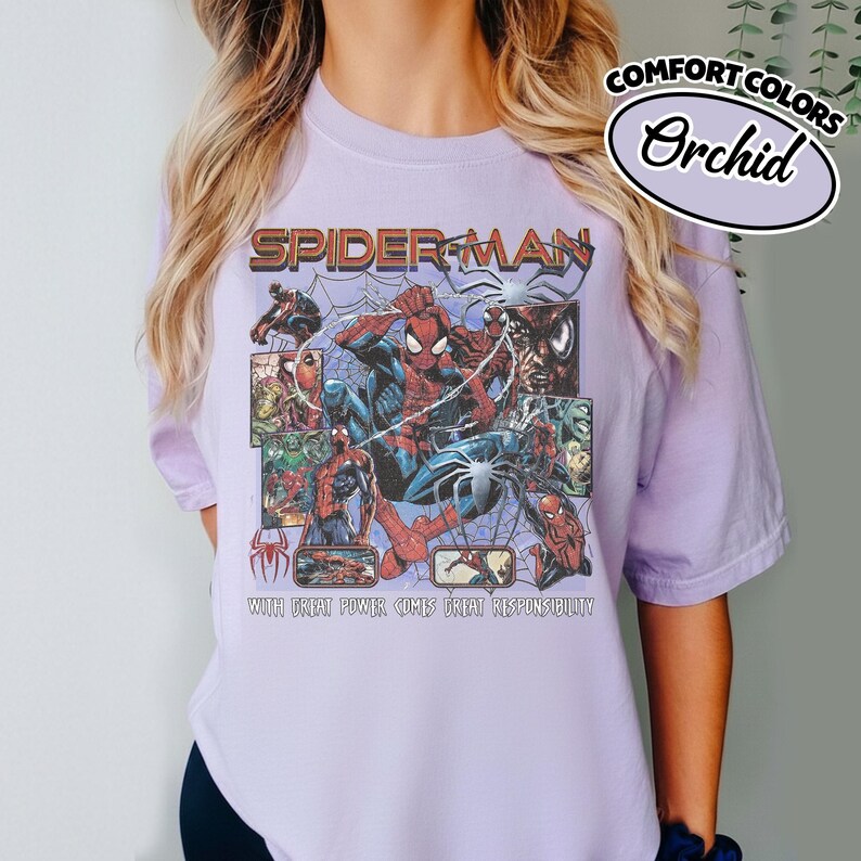 K&ouml;nnte beinhalten: Helllila T-Shirt mit Spider-Man-Grafik. Die Grafik enth&auml;lt die W&ouml;rter "SPIDER-MAN" und "WITH GREAT POWER COMES GREAT RESPONSIBILITY". Das Shirt hat auch die W&ouml;rter "COMFORT COLORS" und "Orchid" aufgedruckt.