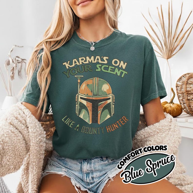 May include: A Blue Spruce Comfort Colors t-shirt with the text "Karma's on Your Scent Like a Bounty Hunter" and a graphic of a Mandalorian helmet. The shirt is a dark teal color.