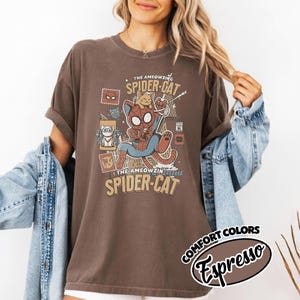 May include: Brown t-shirt featuring a cartoon Spider-Cat design. The graphic includes a cat in a Spider-Man suit, the words "The AMEOWZING SPIDER-CAT" and "COMFORT COLORS Espresso". The shirt has rolled-up sleeves.