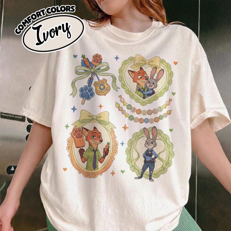 May include: An ivory t-shirt featuring Zootopia character graphics. The design includes a paw print badge, a carrot pen, and framed illustrations of Nick Wilde and Judy Hopps. The text reads COMFORT COLORS IVORY and WELCOME TO ZOOTOPIA.