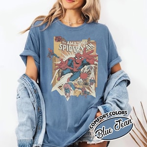 K&ouml;nnte beinhalten: Blaues T-Shirt mit einem Vintage-Comic-Grafik von Spider-Man. Die Grafik enth&auml;lt den Text "The Amazing Spider-Man" und andere Comic-Elemente. Das Shirt ist von der Marke Comfort Colors in der Farbe Blue Jean.
