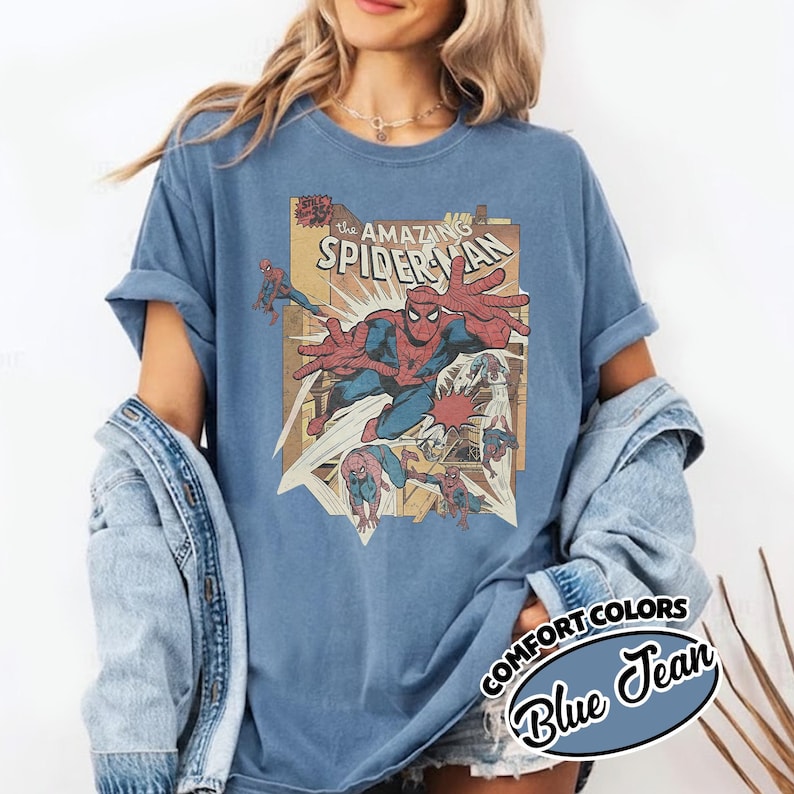 K&ouml;nnte beinhalten: Blaues T-Shirt mit einem Vintage-Comic-Grafik von Spider-Man. Die Grafik enth&auml;lt den Text "The Amazing Spider-Man" und andere Comic-Elemente. Das Shirt ist von der Marke Comfort Colors in der Farbe Blue Jean.