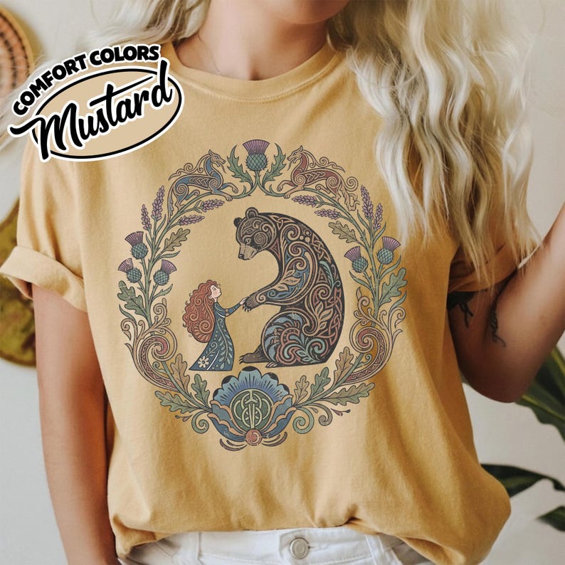 May include: Mustard-colored t-shirt with a circular graphic featuring a bear and a person holding hands, surrounded by a floral wreath. The bear has intricate tribal-style patterns. The text "COMFORT COLORS" and "Mustard" are in the upper left corner.
