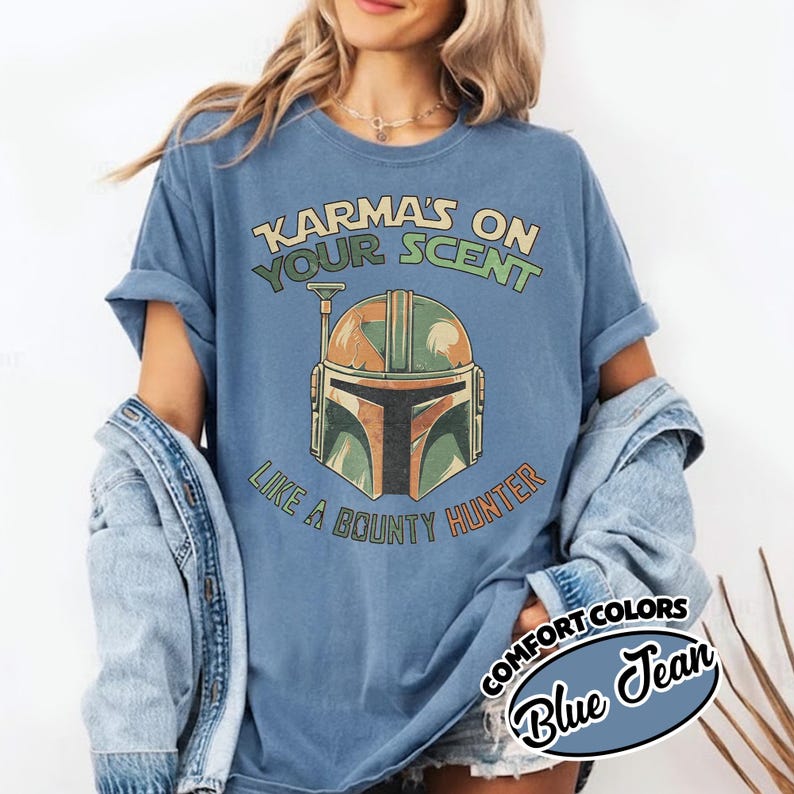 May include: Blue Comfort Colors t-shirt with the text "Karma's on Your Scent Like a Bounty Hunter" and a graphic of a Mandalorian helmet in orange, green, and brown. The shirt is labeled "Blue Jean".