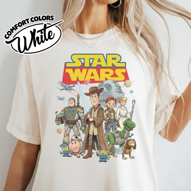 May include: White Comfort Colors t-shirt featuring a Star Wars graphic with characters from Toy Story. The design includes Woody, Buzz Lightyear, and other characters with the Star Wars logo in yellow and red.