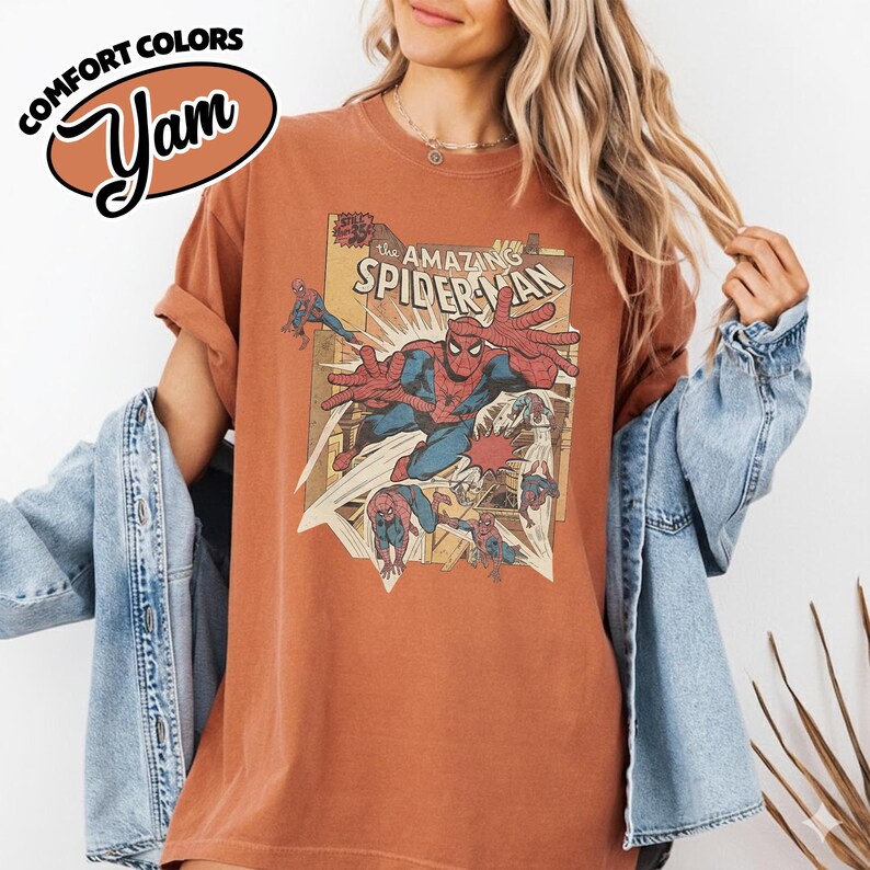 K&ouml;nnte beinhalten: Rostfarbenes T-Shirt mit einem Vintage-Comic-Grafik von Spider-Man. Das Shirt hat hochgekrempelte &Auml;rmel und den Text "COMFORT COLORS" und "Yam" in einem Logo oben links. The Amazing Spider-Man ist die Hauptgrafik.