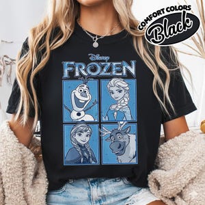 May include: Black t-shirt featuring the Disney Frozen logo and character illustrations of Olaf, Elsa, Anna, and Sven in blue frames. The shirt also has the words "COMFORT COLORS" and "Black" in a circular design.