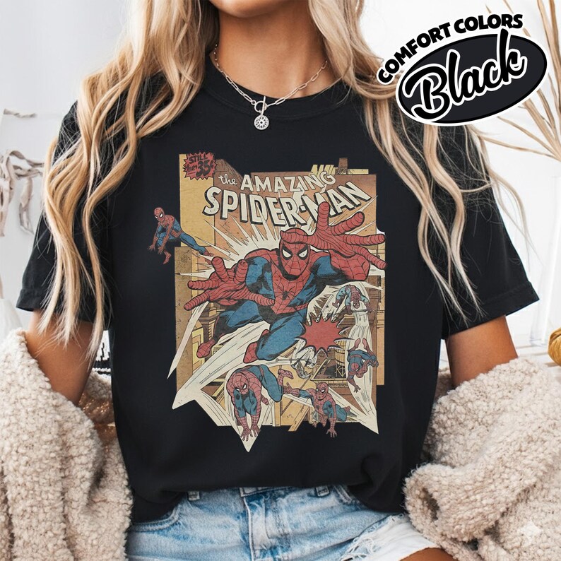 K&ouml;nnte beinhalten: Schwarzes T-Shirt mit einem Vintage-Comic-Cover-Design von Spider-Man. Die Grafik enth&auml;lt den Text "The Amazing Spider-Man" und andere Comic-Elemente. Das T-Shirt ist mit "Comfort Colors Black" gekennzeichnet.