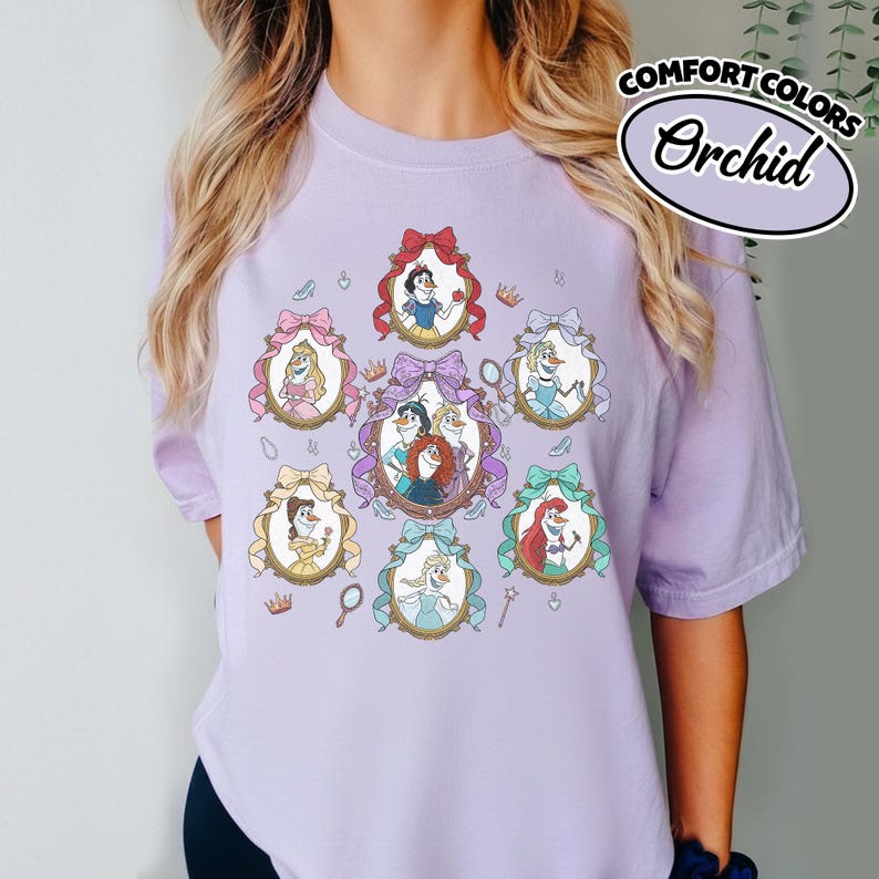 May include: A light purple t-shirt featuring a design of several cartoon princesses in oval frames with bows. The shirt has the words "COMFORT COLORS" and "Orchid" in a white and black oval.