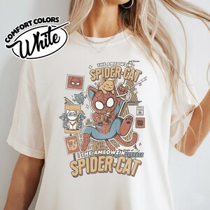 May include: White Comfort Colors t-shirt featuring a comic-style illustration of a cat dressed as Spider-Man, with the text "THE AMEOWZING SPIDER-CAT" and "Origin of the AMEOWZIN GRARKER". The design includes various cat-themed comic book elements.