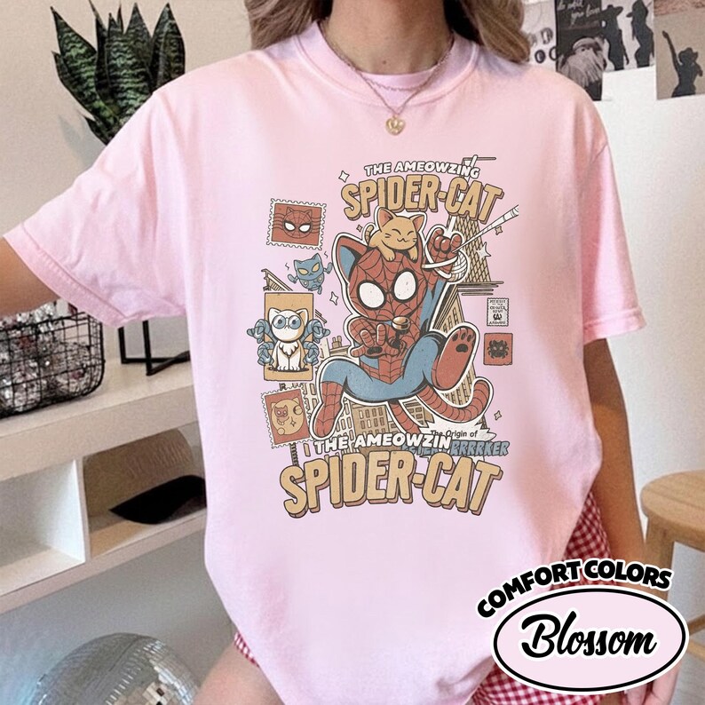 May include: Pink Comfort Colors t-shirt with a graphic of a cat dressed as Spider-Man, with the text "THE AMEOWZING SPIDER-CAT" and "SPIDER-CAT BREAKER". The shirt also has the text "COMFORT COLORS Blossom".