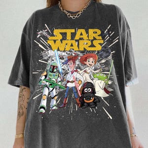 Puede incluir: Camiseta gris oscuro con el logotipo de Star Wars y personajes de dibujos animados como Boba Fett, Woody, Jessie, Darth Vader y un extraterrestre. La camiseta est&aacute; estampada con un efecto desgastado y el texto "Pepper Comfort Colors".
