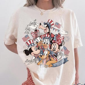 Puede incluir: Camiseta Comfort Colors color marfil con un dise&ntilde;o patri&oacute;tico con Mickey Mouse, Minnie Mouse, Donald Duck, Daisy Duck, Goofy y Pluto. El gr&aacute;fico incluye banderas americanas y texto que celebra el 250 aniversario de Am&eacute;rica.
