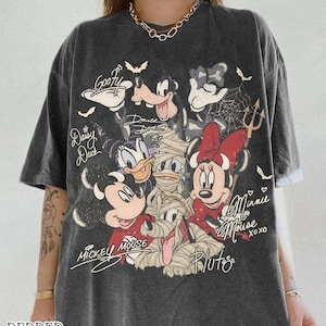 May include: Dark grey t-shirt with a graphic of Disney characters, including Mickey Mouse, Minnie Mouse, Donald Duck, and Goofy. The design includes bats, spiderwebs, and the text "Mickey Mouse" and "Minnie Mouse". The shirt also has the text "Pepper Comfort Colors".