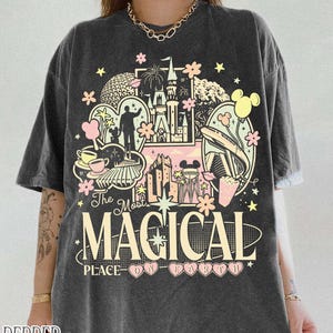 May include: Dark grey t-shirt with a colourful graphic design featuring a castle, Mickey Mouse, and the text "The Most Magical Place on Earth." The shirt has a vintage look.