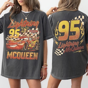 Puede incluir: Camiseta gris oscuro con Lightning McQueen de la pel&iacute;cula Cars. El gr&aacute;fico frontal muestra a McQueen con el n&uacute;mero 95, una bandera a cuadros y el texto "Lightning McQueen". La parte posterior de la camiseta tambi&eacute;n muestra "95" y "Lightning McQueen".