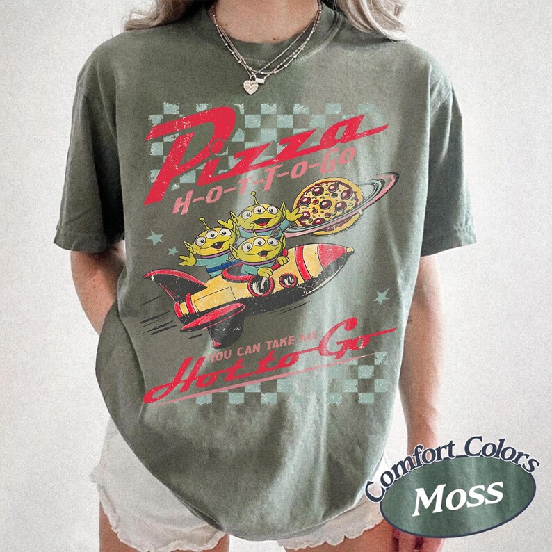Pu&ograve; includere: T-shirt verde oliva con una grafica raffigurante tre alieni dei cartoni animati su un razzo, una pizza e la scritta "Pizza H-O-T-O". La maglietta ha anche la scritta "You can take me H-O-T-O Go".