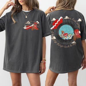 May include: A charcoal grey short-sleeve t-shirt featuring a small graphic on the front left chest and a large graphic on the back. Both graphics depict a red cowboy boot and the text "Love has a way of bringing things back to life."