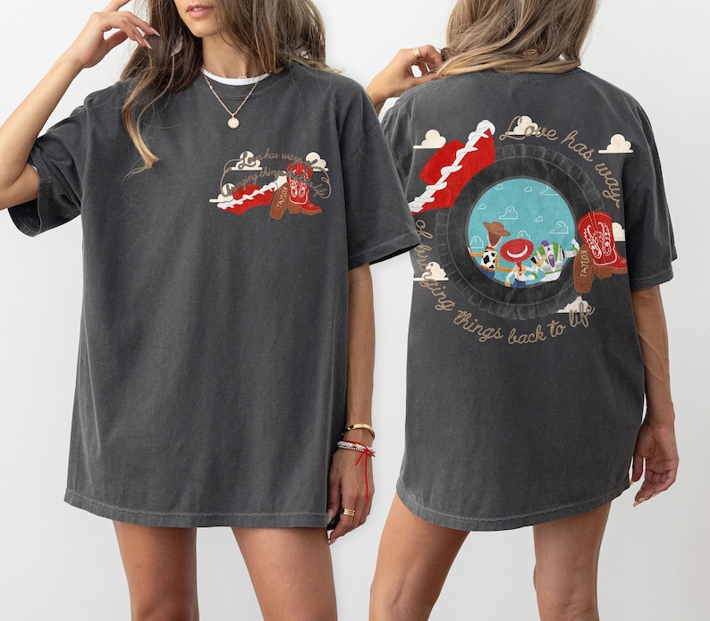 May include: A charcoal grey short-sleeve t-shirt featuring a small graphic on the front left chest and a large graphic on the back. Both graphics depict a red cowboy boot and the text "Love has a way of bringing things back to life."