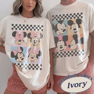 May include: Ivory-colored t-shirts featuring Mickey and Minnie Mouse designs. The shirts have a checkerboard pattern and are paired with red and white checkered shorts. The text "Comfort Colors Ivory" is visible.