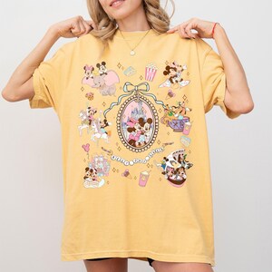 May include: Yellow t-shirt featuring a colorful graphic of Disney characters and attractions. The design includes Mickey and Minnie Mouse, Dumbo, and a castle, with the text "Best Days Ever".