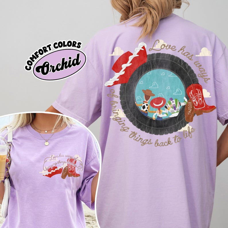 May include: A light purple t-shirt featuring a graphic on the back and front. The back graphic shows a tyre framing cartoon characters, a red hat, and a red cowboy boot with the text Love has ways of bringing things back to life.
