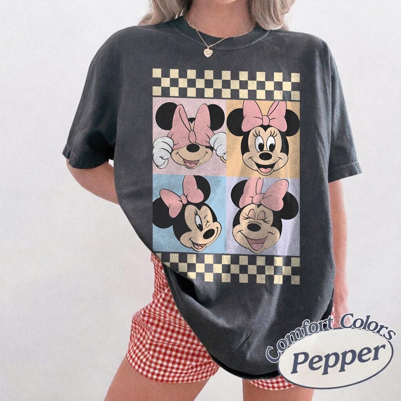 May include: Dark gray t-shirt featuring four panels with Minnie Mouse faces, each with a pink bow. The design includes a checkered border and pastel color blocks. The shirt has the text "Comfort Colors Pepper" on the bottom right.