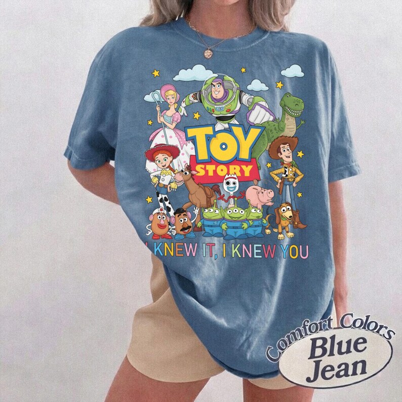 May include: A blue short-sleeve t-shirt featuring a graphic print of Toy Story characters including Buzz Lightyear, Woody, Jessie, and the Aliens. The text reads TOY STORY and I KNEW IT, I KNEW YOU. The shirt has a crew neckline and a relaxed fit.