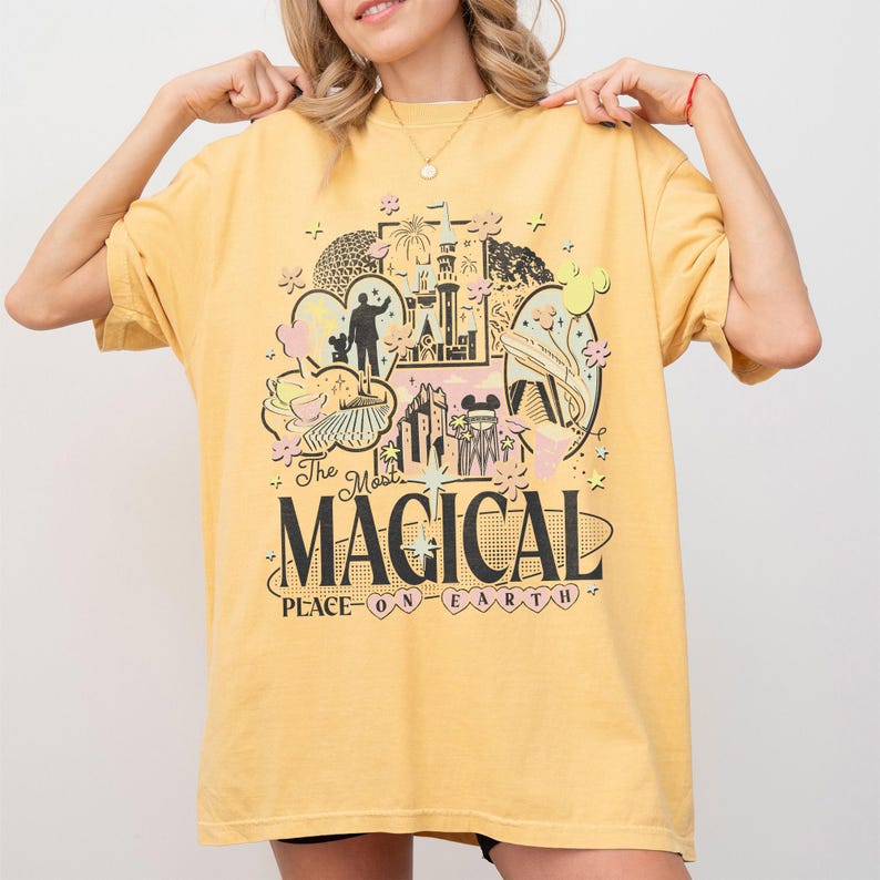 May include: Mustard yellow t-shirt with a colourful graphic design featuring a castle, Mickey Mouse, and the text "The Most Magical Place on Earth." The shirt has short sleeves and a relaxed fit.