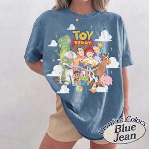 May include: A blue short-sleeve t-shirt featuring a graphic print of Toy Story characters including Woody, Buzz Lightyear, Rex, and Jessie. The design includes white clouds, yellow stars, and the red and yellow Toy Story logo text.