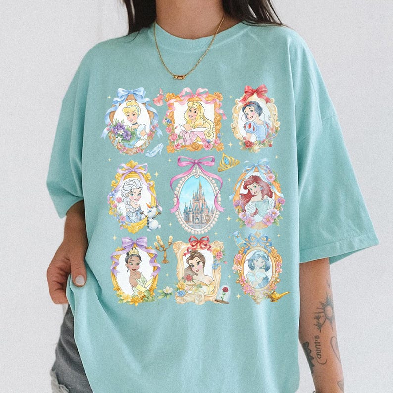 Pu&ograve; includere: Una maglietta azzurra con ritratti incorniciati di principesse animate. Ogni ritratto &egrave; circondato da dettagli floreali e fiocchi. Il design include un castello, una scarpetta di cristallo e una corona.