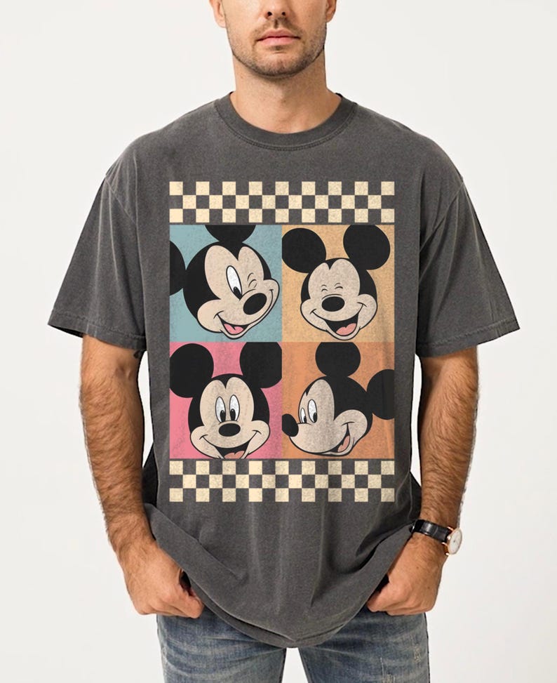 May include: Dark gray t-shirt featuring a colorful graphic of Mickey Mouse's face in four squares. The squares are in blue, orange, pink, and beige, with a checkered border. The shirt has a vintage, worn look.